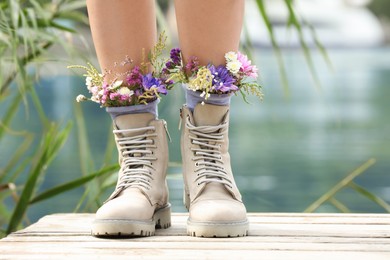 Photo of Woman standing on wooden pier with flowers in socks outdoors, closeup
