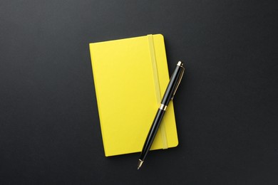 Photo of Closed yellow notebook and pen on black background, top view