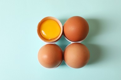 Cracked and whole chicken eggs on light blue background, flat lay