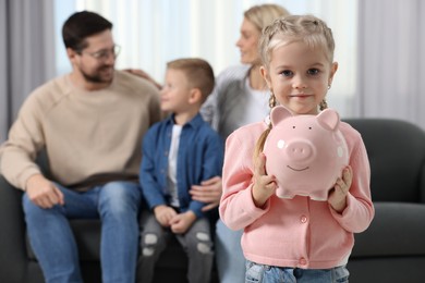 Photo of Family budget. Little girl with piggy bank, her parents and brother at home, selective focus