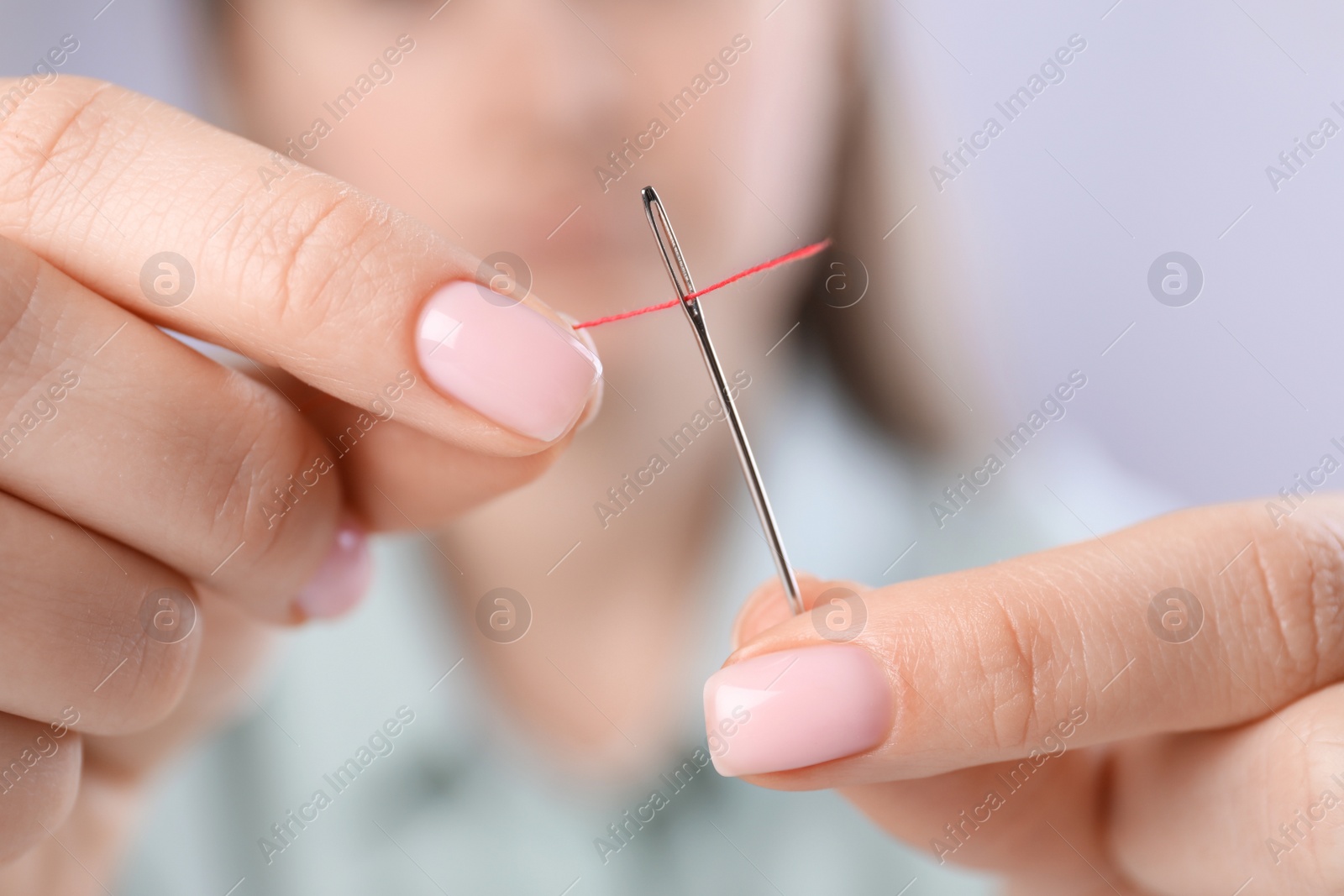 Photo of Woman threading needle, closeup view. Sewing equipment