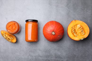 Photo of Jars of pumpkin jam and fresh pumpkins on grey table, flat lay