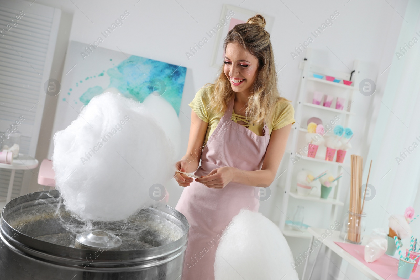 Photo of Young woman making cotton candy using modern machine indoors