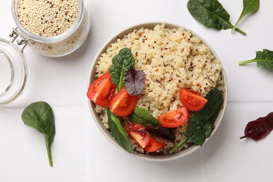 Photo of Tasty quinoa porridge with tomatoes and spinach in bowl on white tiled table, flat lay