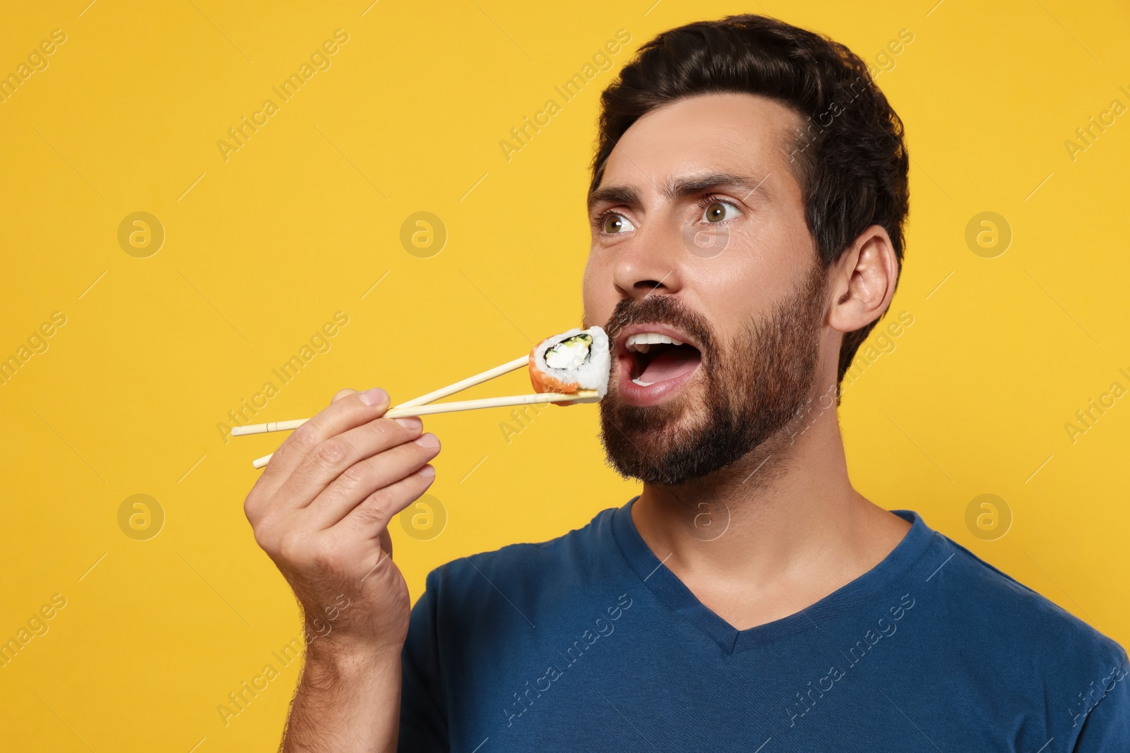 Photo of Handsome man eating sushi roll with chopsticks on orange background