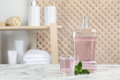 Photo of Bottle and glass with mouthwash on white marble table in bathroom, space for text
