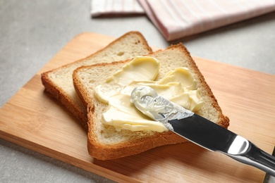 Photo of Spreading butter onto toast with knife on wooden board