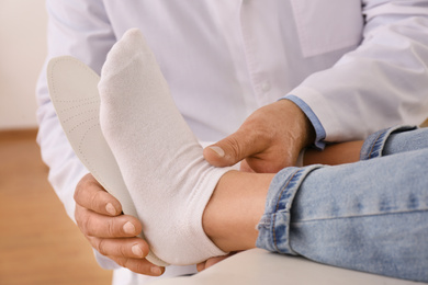 Male orthopedist fitting insole on patient's foot in clinic, closeup