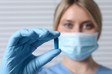 Doctor holding pill on light background, selective focus