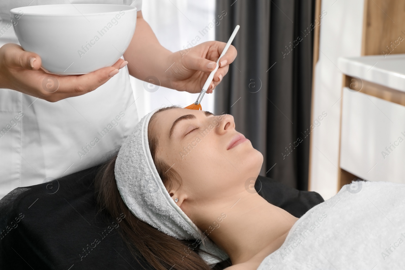 Photo of Cosmetologist with brush applying cosmetic product to client`s face in clinic, closeup