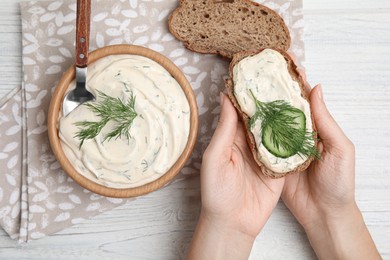 Photo of Woman holding bread with tasty creamy dill sauce at white wooden table, top view