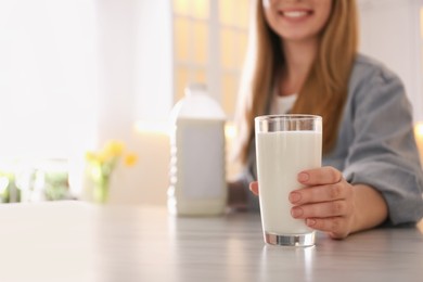 Photo of Young woman with gallon bottle of milk and glass at white marble table in kitchen, closeup. Space for text