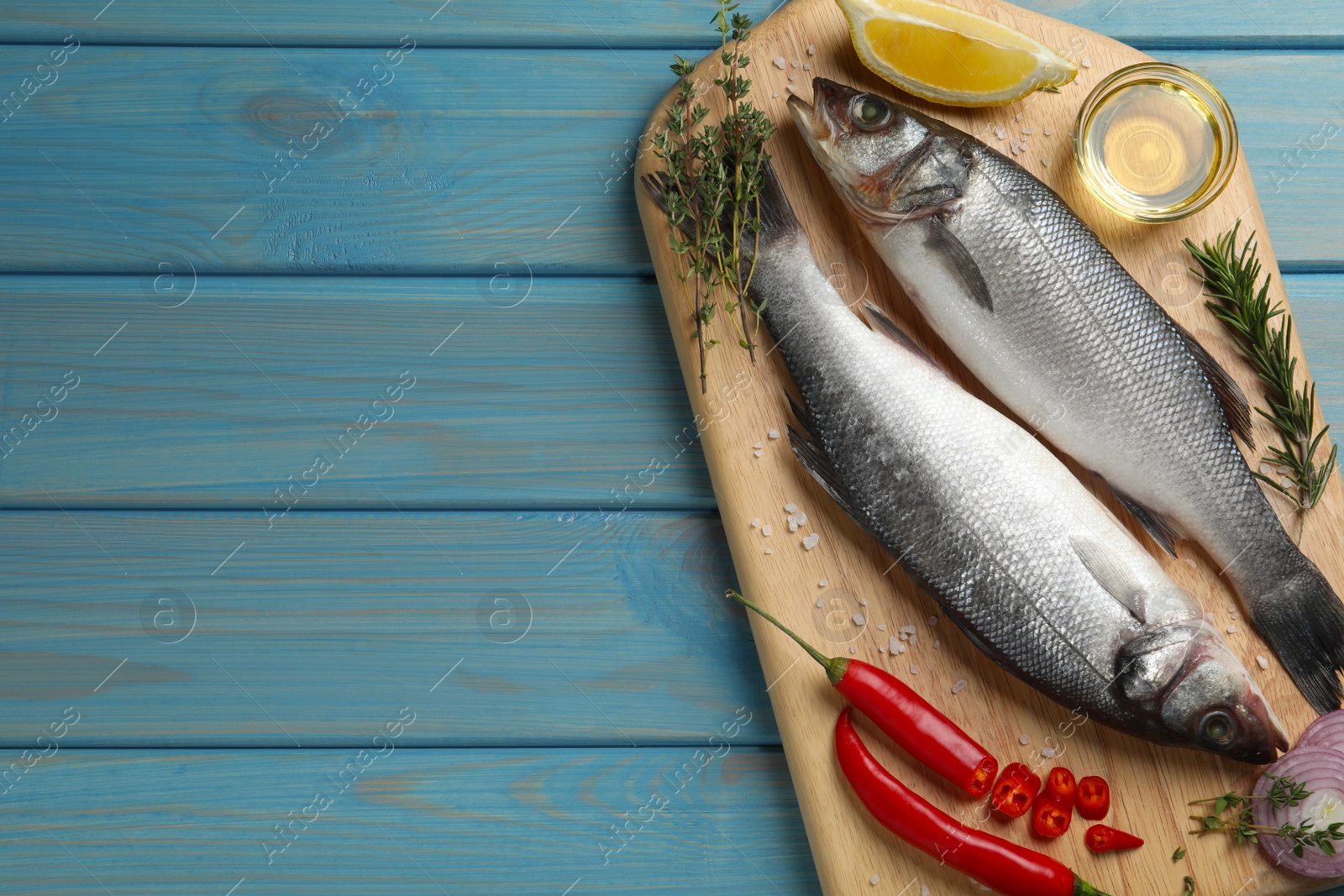 Photo of Sea bass fish and ingredients on light blue wooden table, top view. Space for text