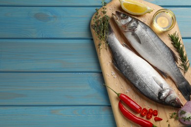 Sea bass fish and ingredients on light blue wooden table, top view. Space for text