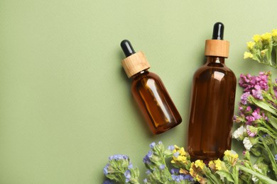 Photo of Bottles of face serum with beautiful flowers on light green background, flat lay. Space for text