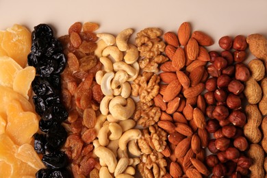 Mix of delicious dried nuts and fruits on beige background, flat lay