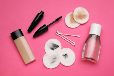 Bottle of makeup remover, dirty cotton pads, buds and different cosmetic products on pink background, flat lay