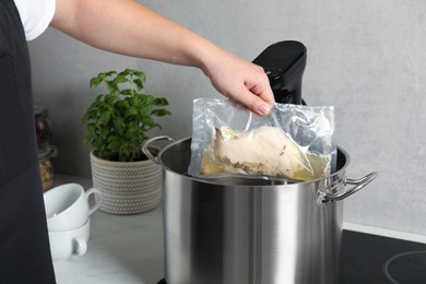 Photo of Woman taking out vacuum packed meat from pot in kitchen, closeup. Thermal immersion circulator for sous vide cooking