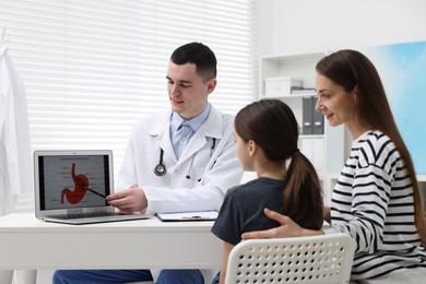 Photo of Gastroenterologist consulting woman with her daughter and showing image of stomach on laptop in clinic