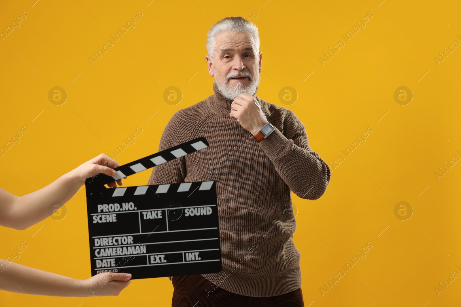 Photo of Senior actor performing while second assistant camera holding clapperboard on yellow background. Film industry