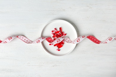 Photo of Plate with weight loss pills and measuring tape on wooden background, top view