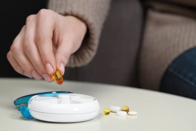 Photo of Woman taking pill from plastic box at white table, closeup. Space for text