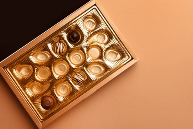 Photo of Partially empty box of chocolate candies on light brown background, top view. Space for text