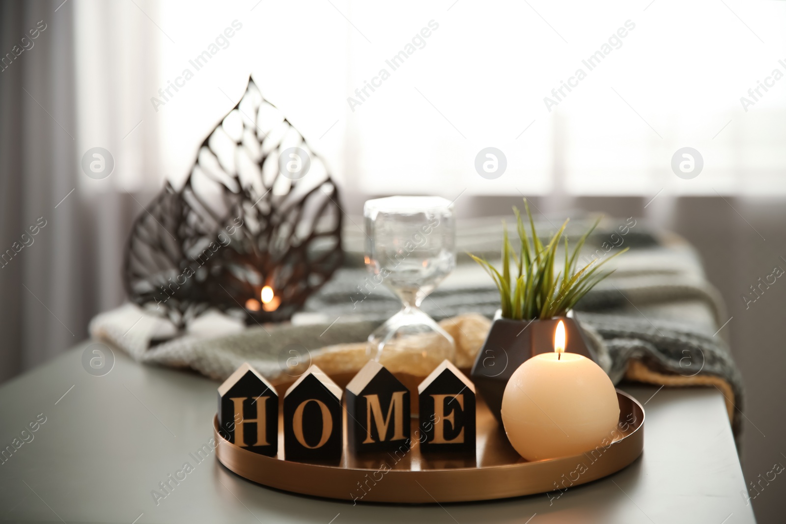 Photo of Tray with burning candle, word HOME and hourglass on table indoors