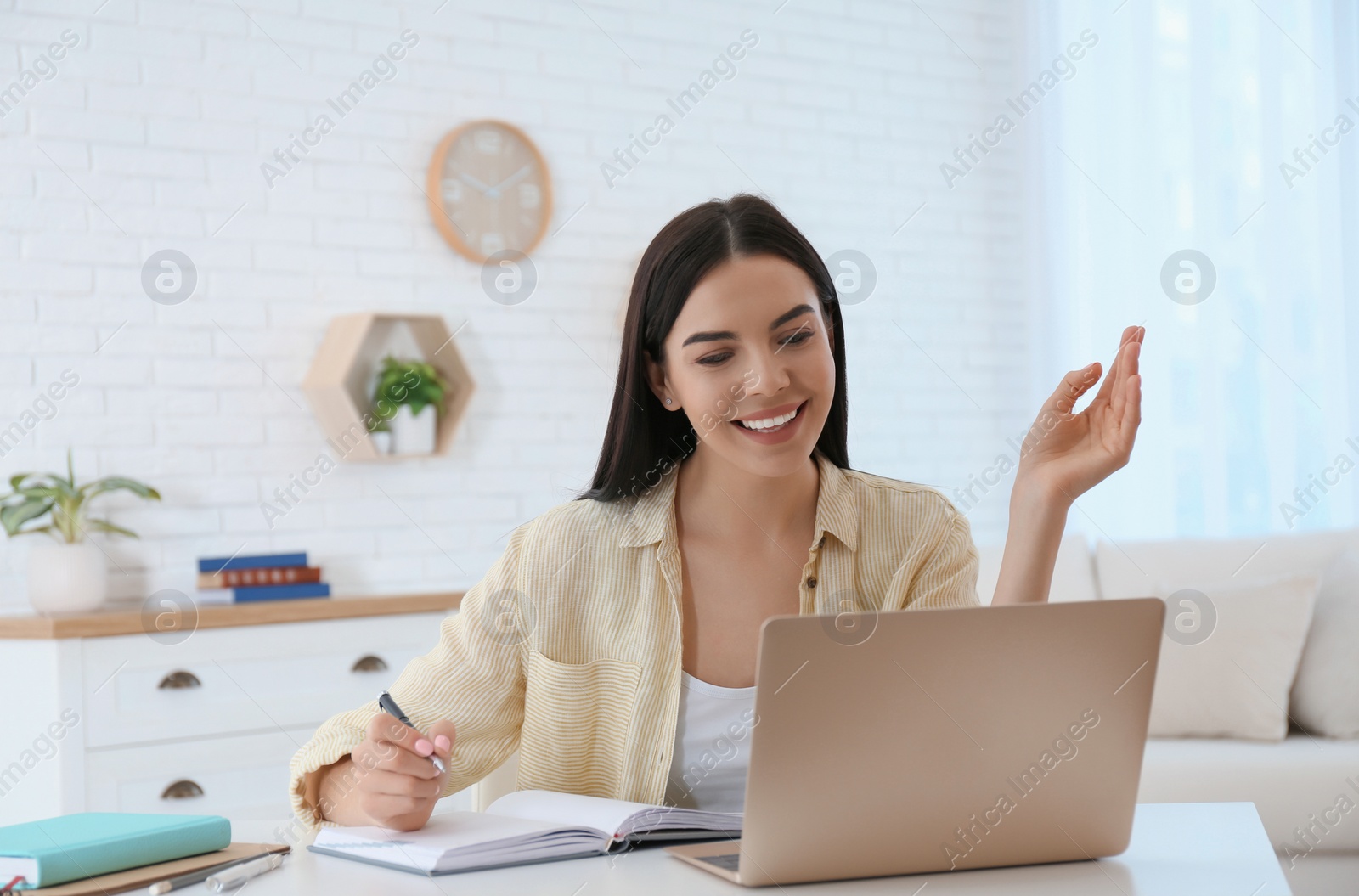 Photo of Young woman taking notes during online webinar at table indoors