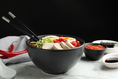 Photo of Delicious ramen in bowl on white marble table against black background, closeup. Noodle soup