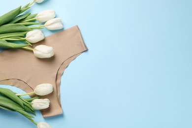 Photo of Beige women's underwear and tulips on light blue background, flat lay. Space for text