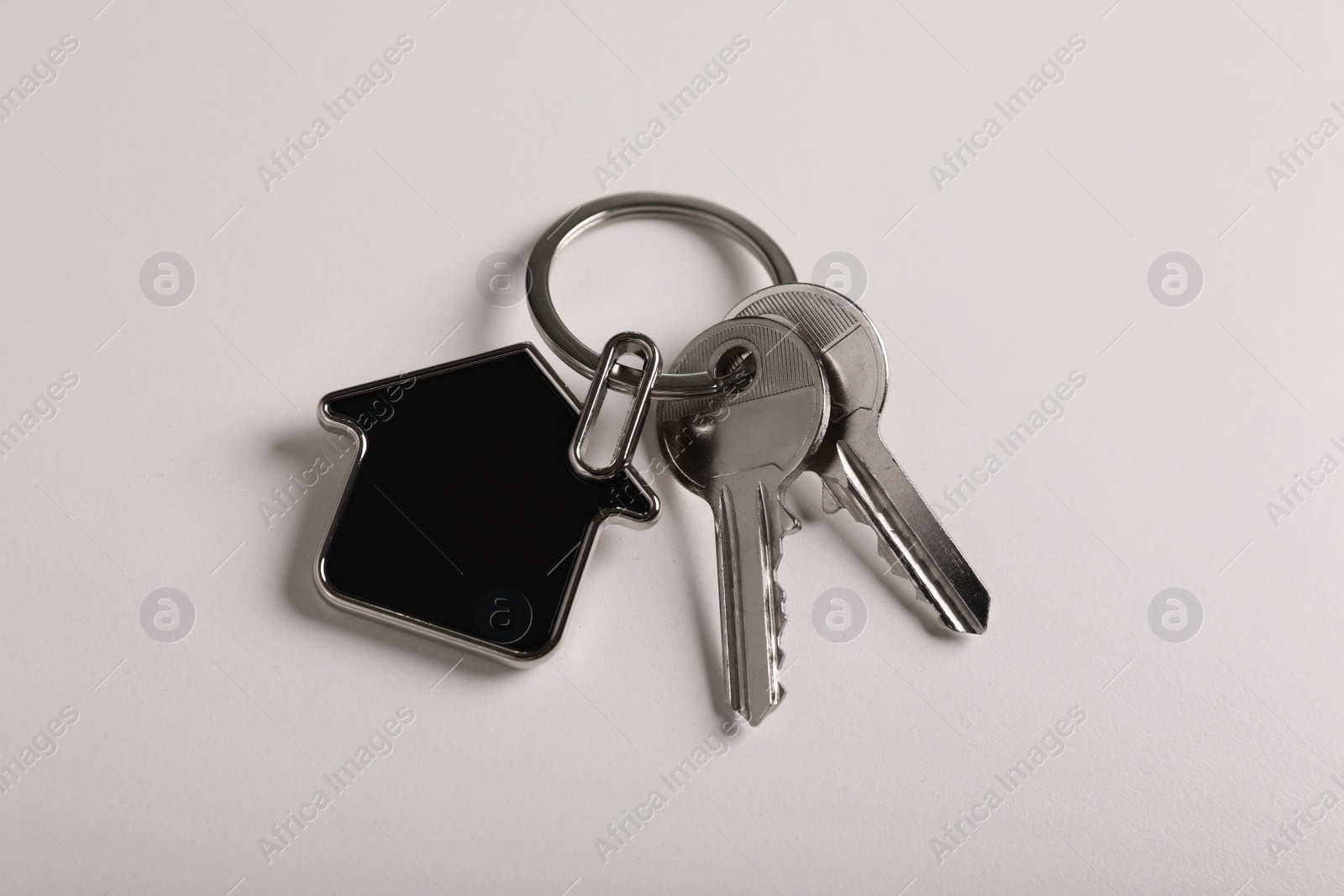 Photo of Keys with trinket in shape of house on white background, above view. Real estate agent services