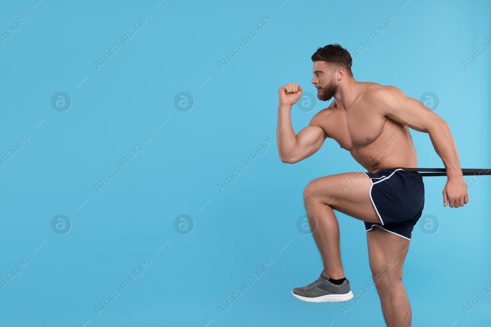 Photo of Young man exercising with elastic resistance band on light blue background. Space for text