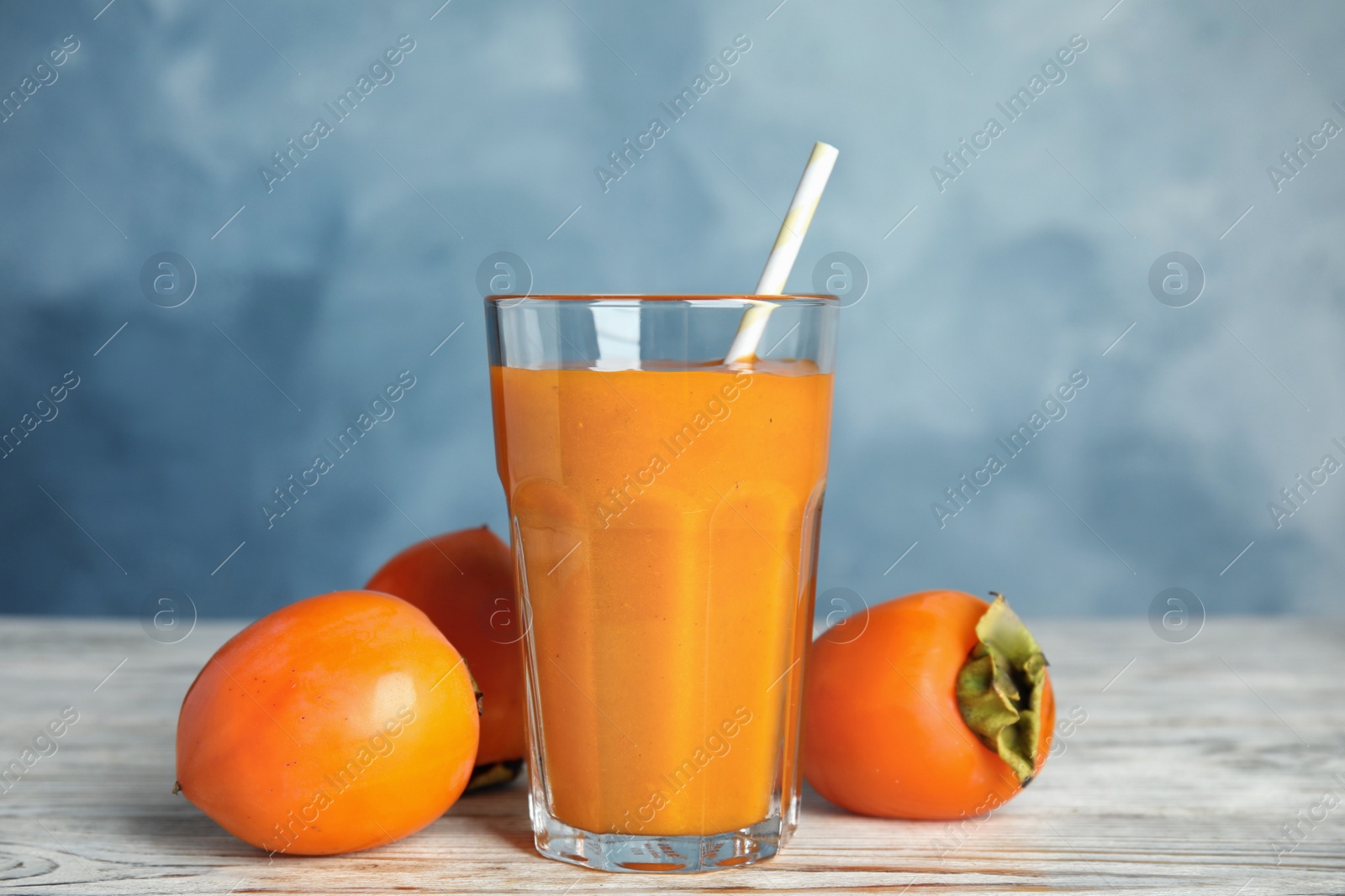 Photo of Fresh tasty persimmon smoothie and fresh fruits on white wooden table against light blue background