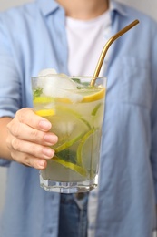 Photo of Woman holding glass of citrus refreshing drink with gold straw, closeup