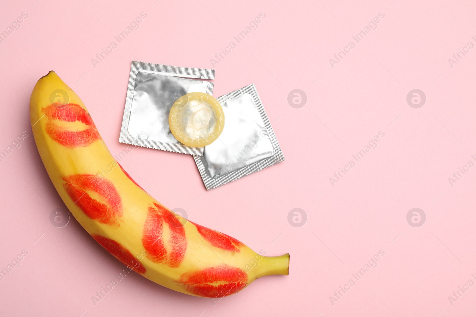 Photo of Condoms, banana with lipstick kiss marks and space for text on pink background, flat lay. Safe sex