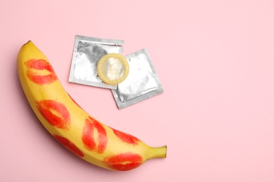 Photo of Condoms, banana with lipstick kiss marks and space for text on pink background, flat lay. Safe sex