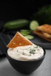 Photo of Tasty creamy dill sauce with cracker in bowl on grey table