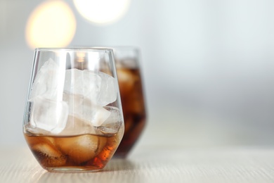 Photo of Glass of cola with ice on table against blurred background. Space for text