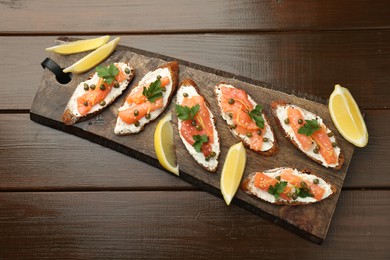 Photo of Tasty canapes with salmon, capers, lemon and cream cheese on wooden table, top view