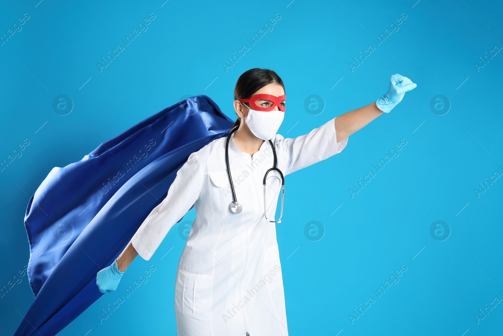 Photo of Doctor dressed as superhero posing on light blue background. Concept of medical workers fighting with COVID-19