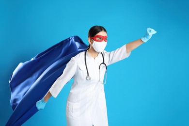 Doctor dressed as superhero posing on light blue background. Concept of medical workers fighting with COVID-19