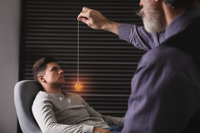 Photo of Psychotherapist using pendulum during hypnotherapy   session in office