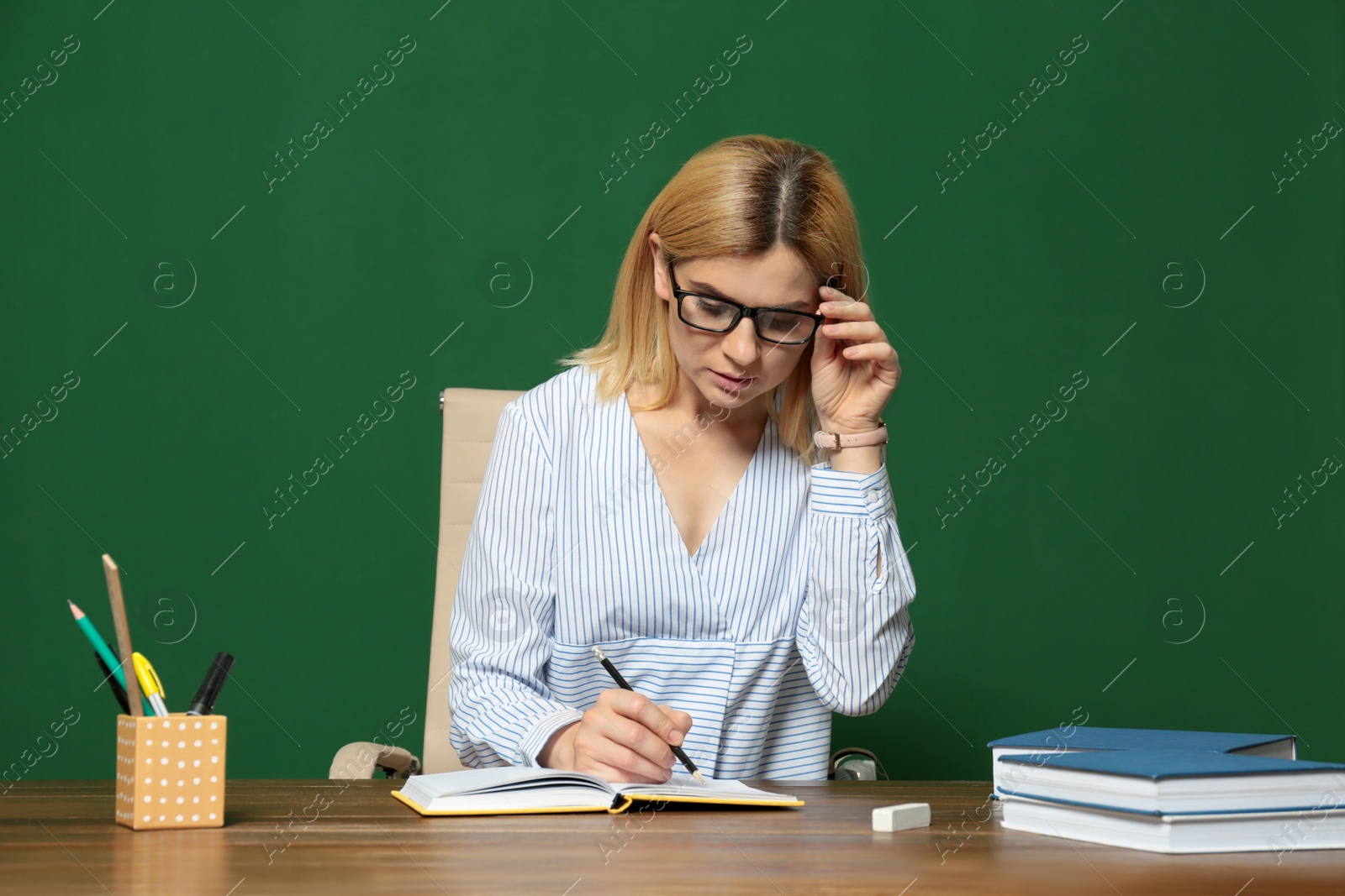 Photo of Portrait of beautiful teacher sitting at table near chalkboard