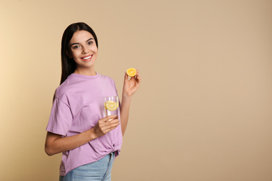Beautiful young woman with tasty lemon water and fresh fruit on beige background. Space for text