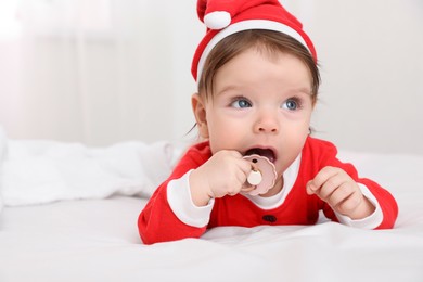Photo of Cute baby wearing festive Christmas costume with pacifier on bed