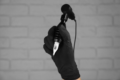 Photo of Professional tattoo artist with machine near white brick wall, closeup