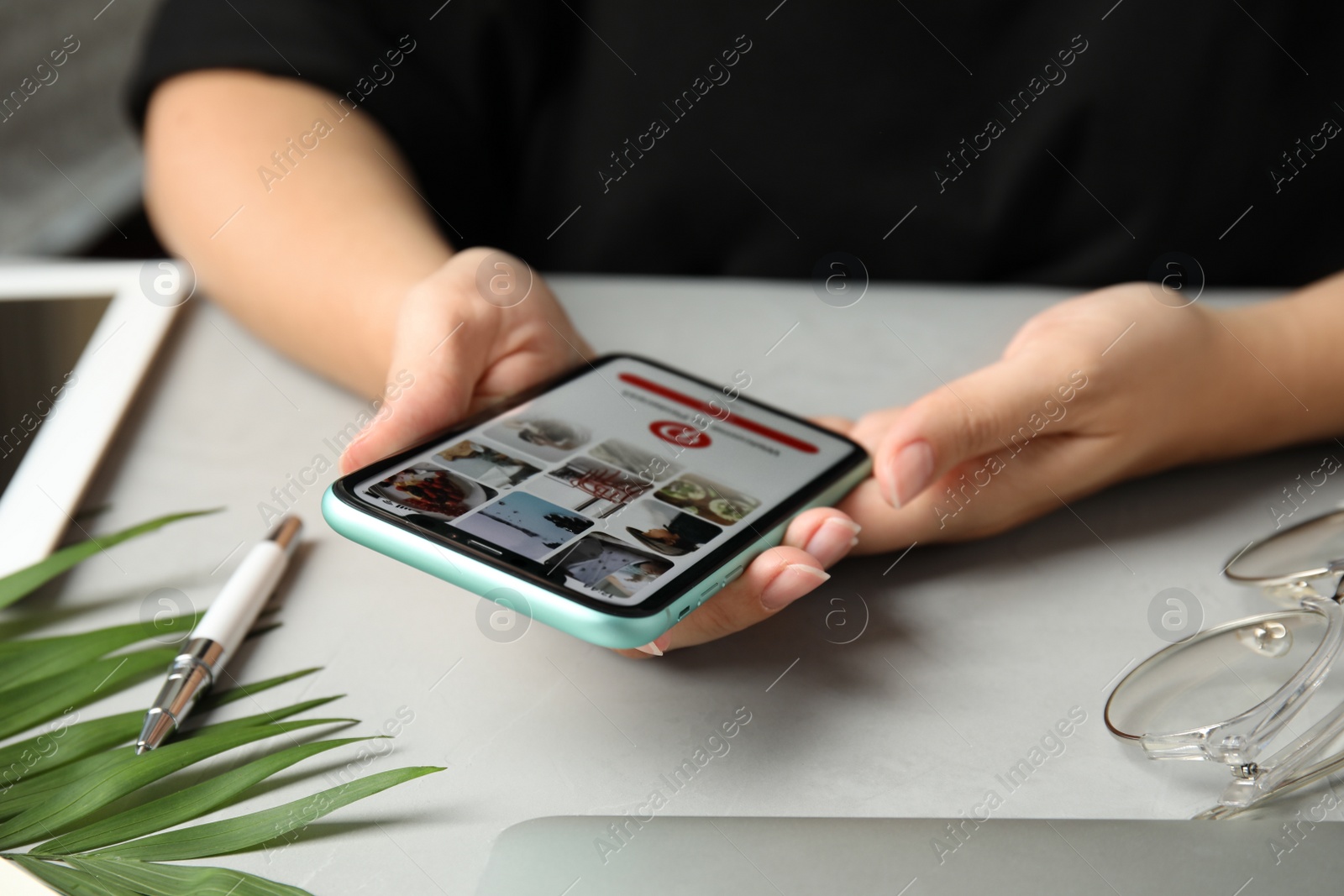 Photo of MYKOLAIV, UKRAINE - JULY 9, 2020: Woman holding Iphone 11 with Pinterest app on screen at table, closeup