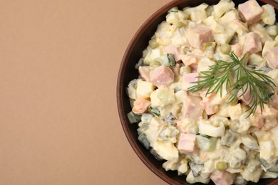 Tasty Olivier salad with boiled sausage in bowl on beige table, top view. Space for text