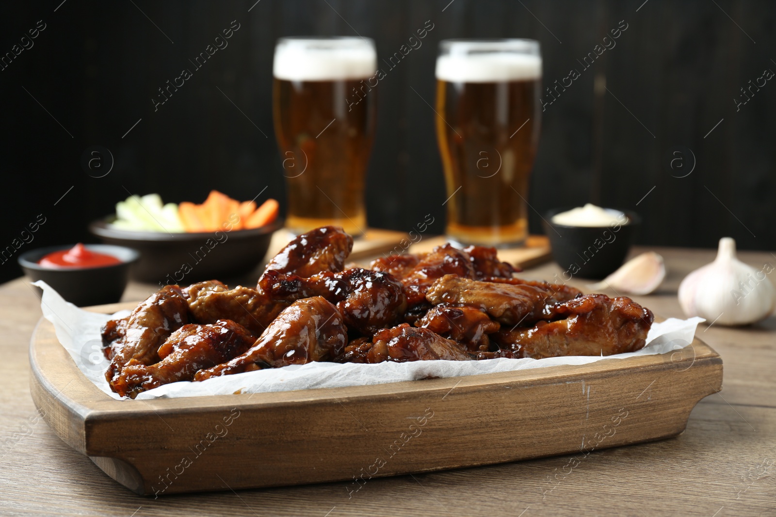 Photo of Tasty chicken wings, sauces, vegetable sticks and glasses of beer on wooden table, closeup. Delicious snacks